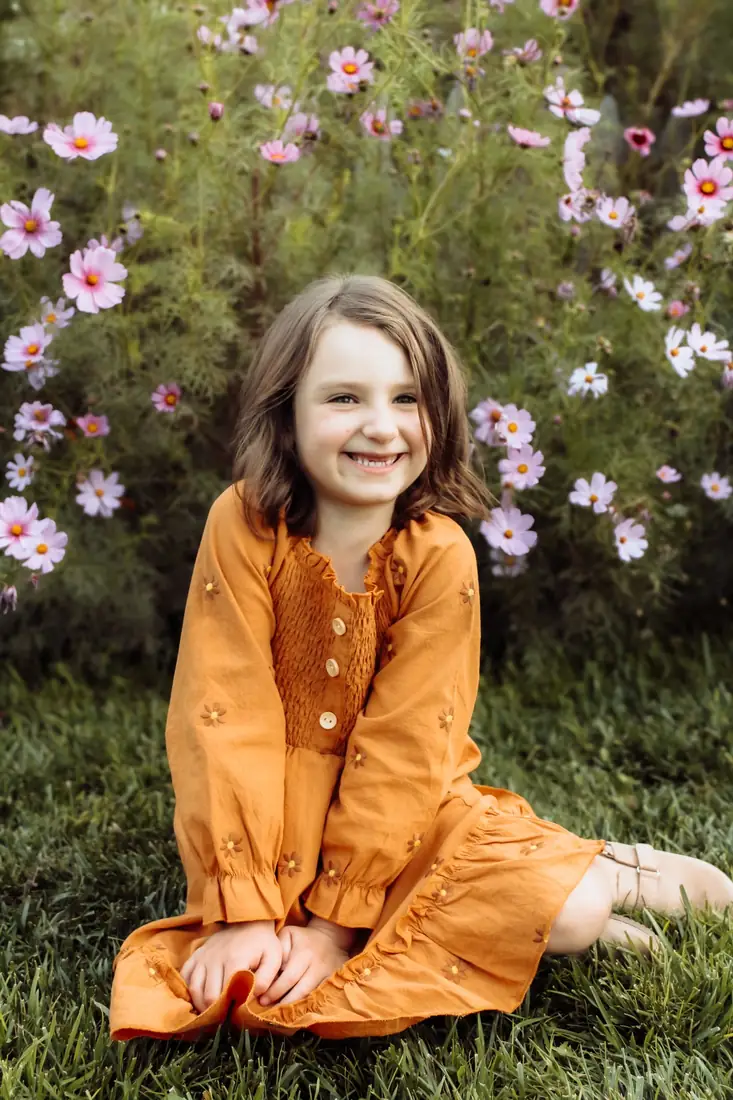Girl in an orange dress laughing in a field of cosmos flowers