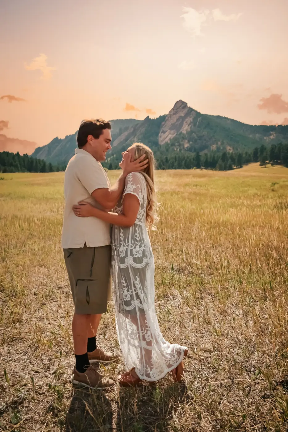 Couple embracing in a golden field at sunset, she laughs up at him