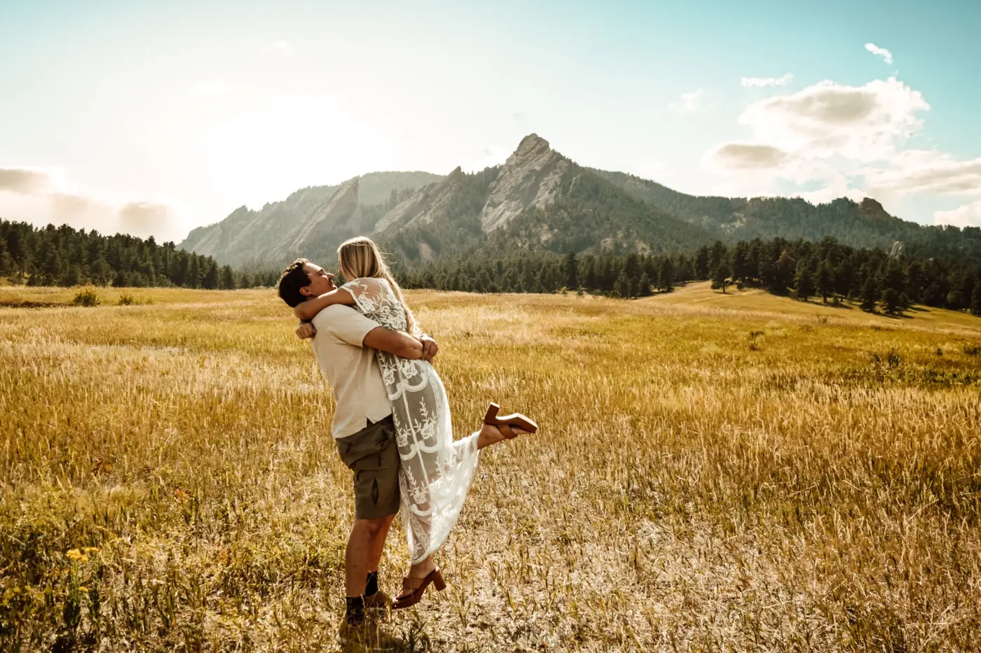 Couple embracing as he lifts her in a golden field below the Flatirons