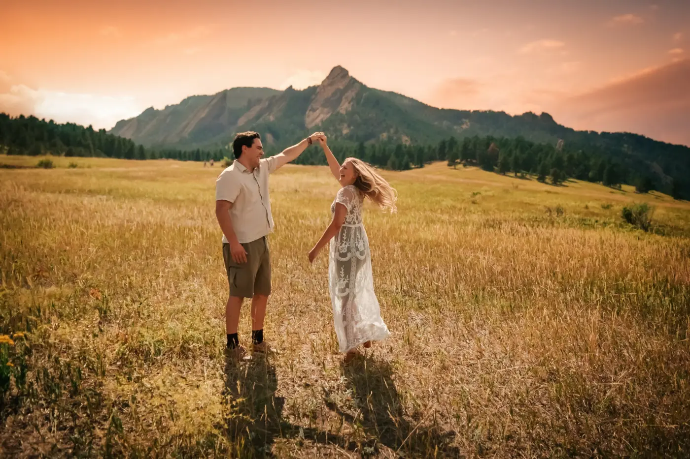 Couple dancing in a golden field with the Flatirons at sunset