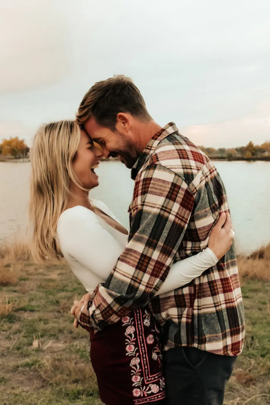 Couple laughing forehead to forehead by the lake at sunset