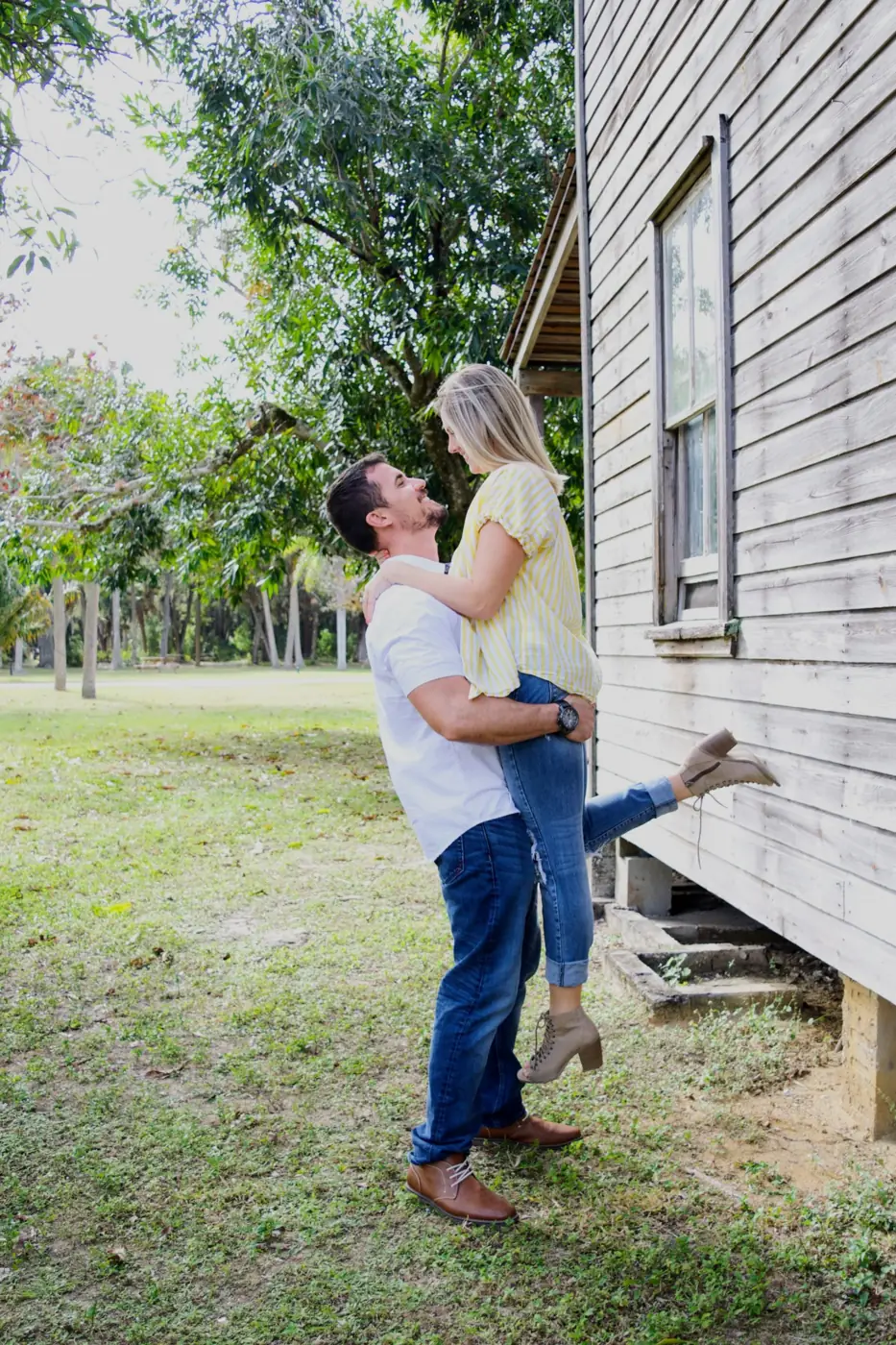 He lifts her off the ground beside an old wooden farmhouse