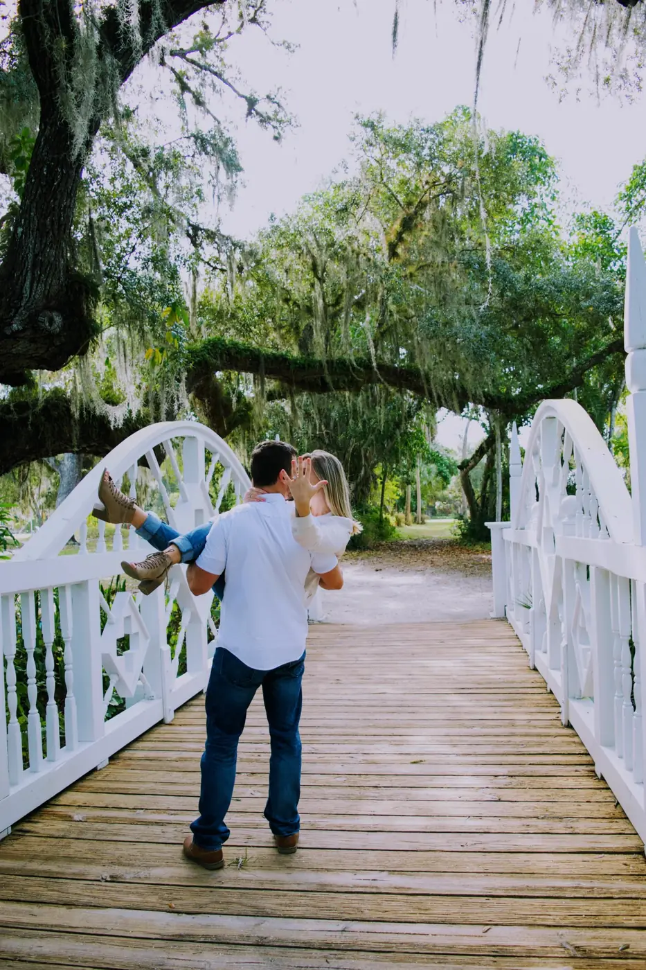 He carries her across a white bridge as she shows her ring