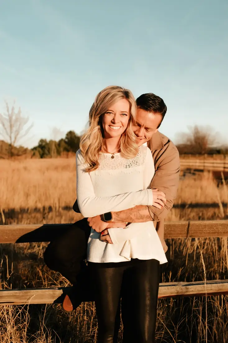 Engaged couple embracing on a wooden fence in a golden field