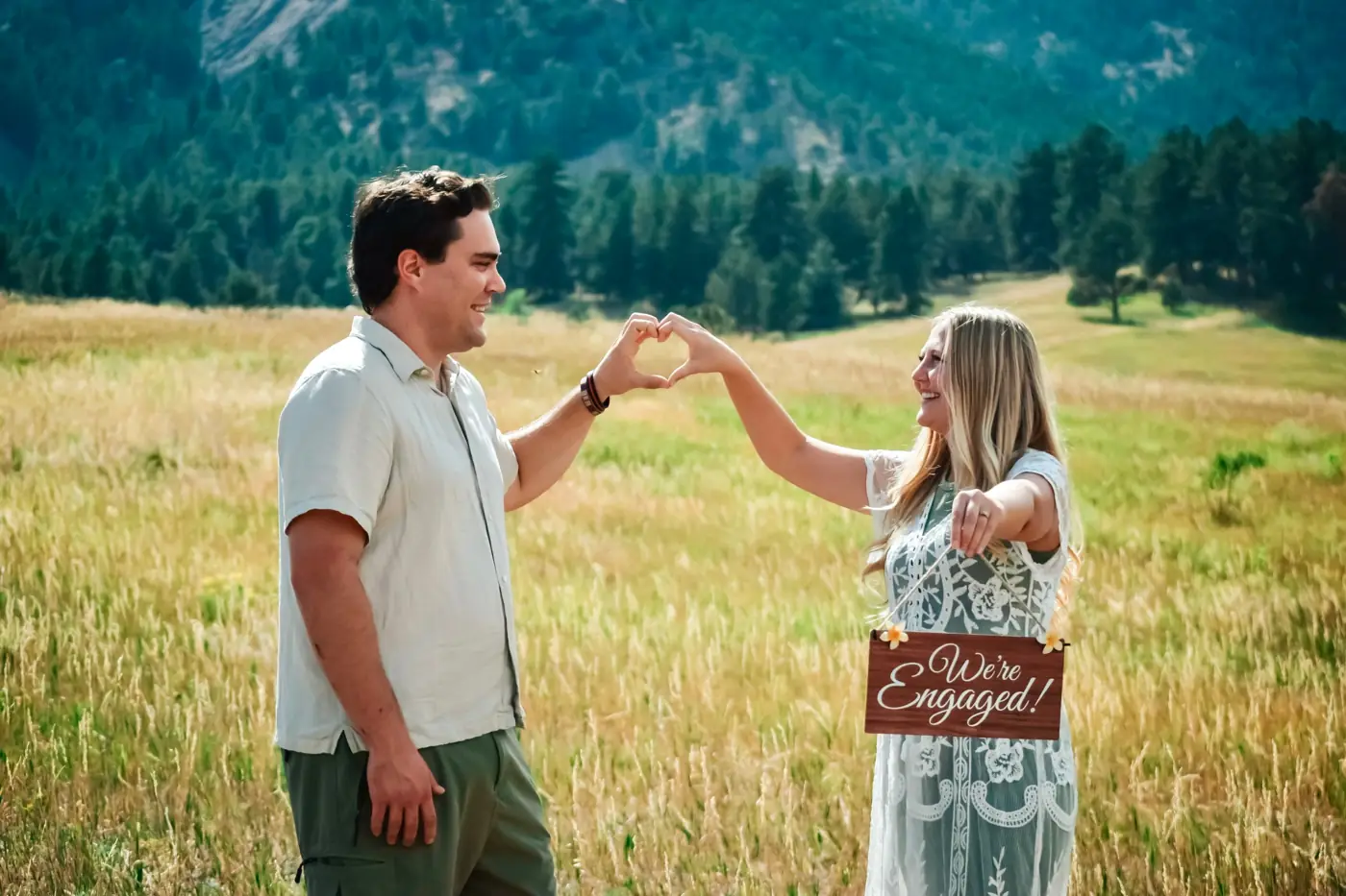 We’re Engaged sign: couple making a heart with their hands in a golden field