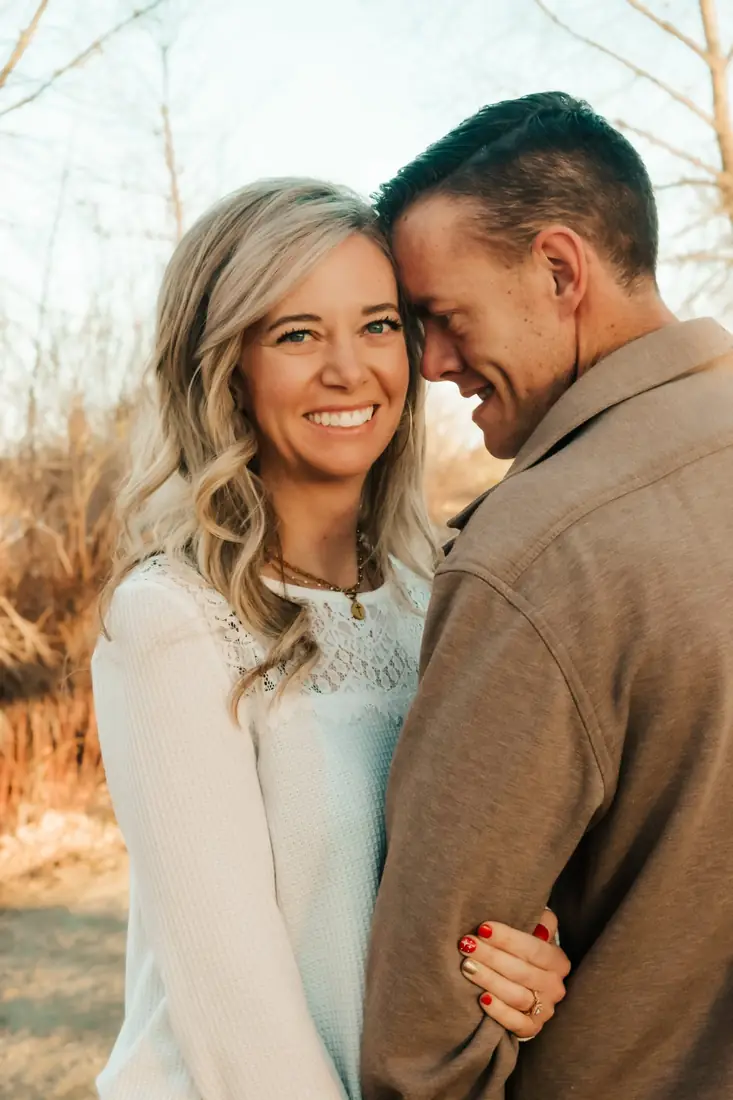 Engaged couple cheek to cheek, she smiles at the camera