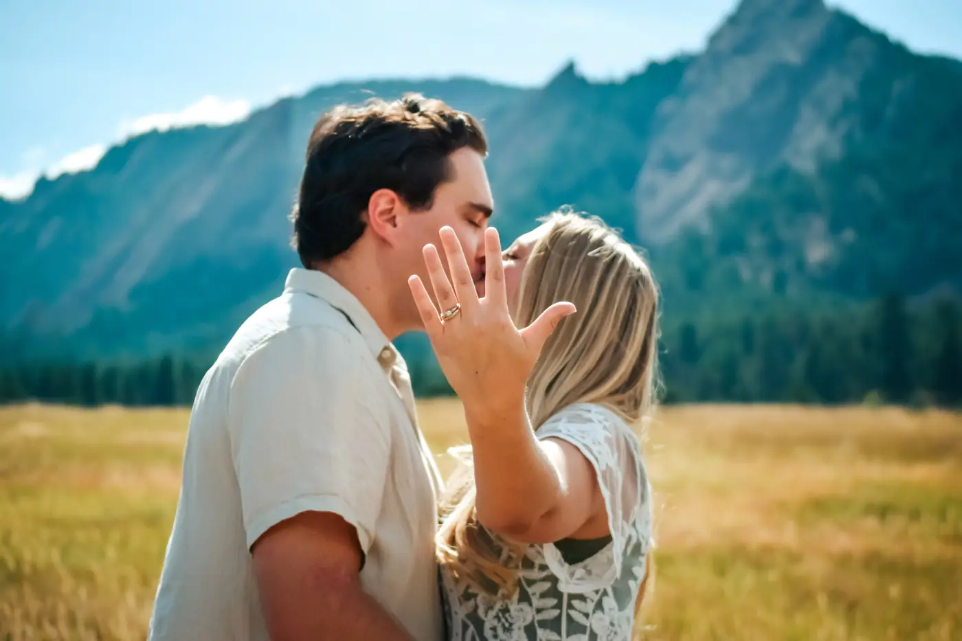 Couple kissing with her engagement ring in the foreground and the Flatirons behind