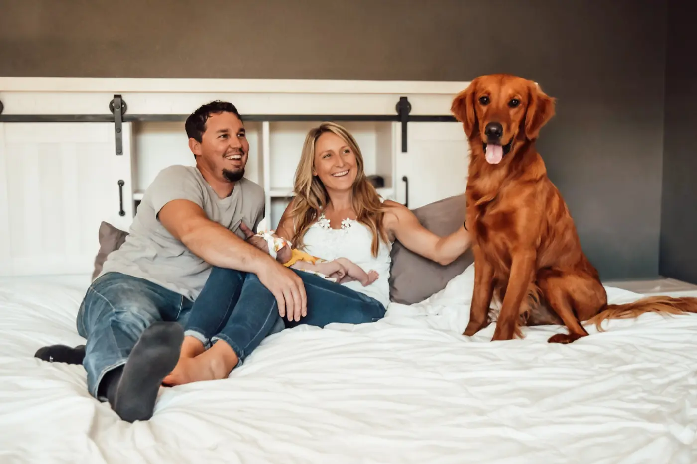 Couple with their newborn and golden retriever on a bed