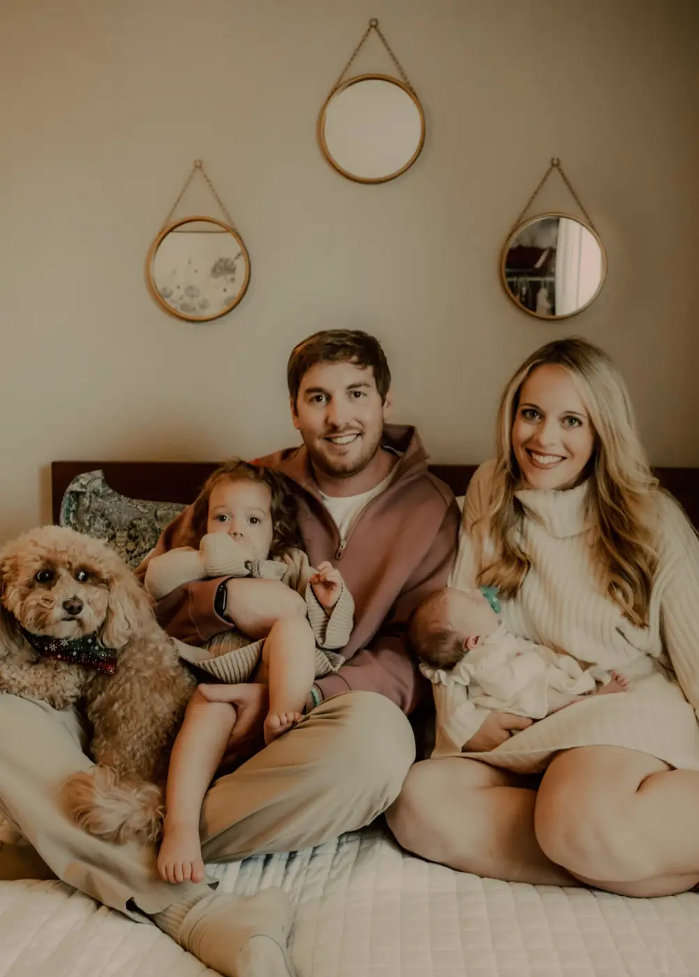 Family with their dog and two little ones sitting on a bed