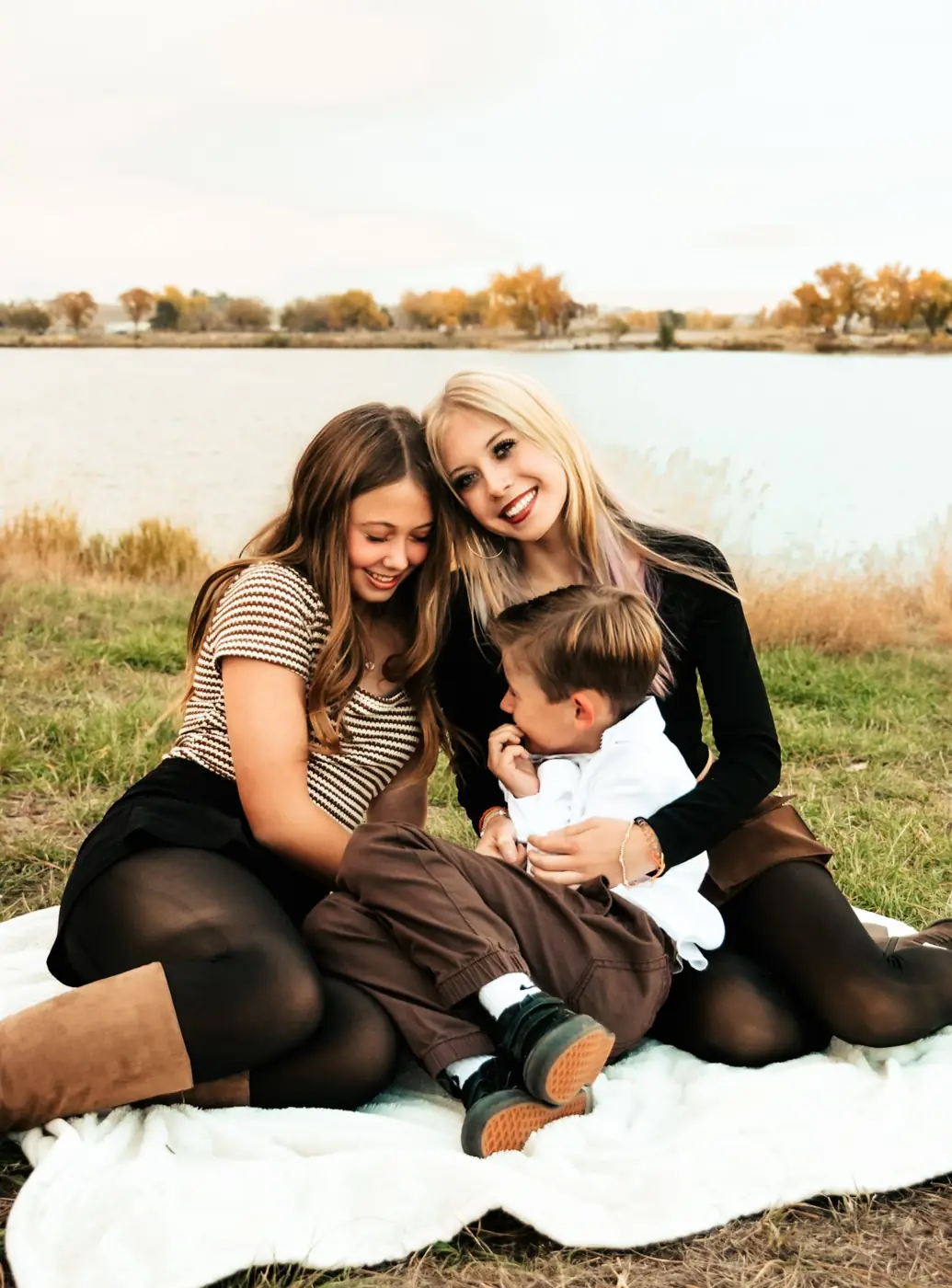 Siblings laughing together on a blanket by the lake