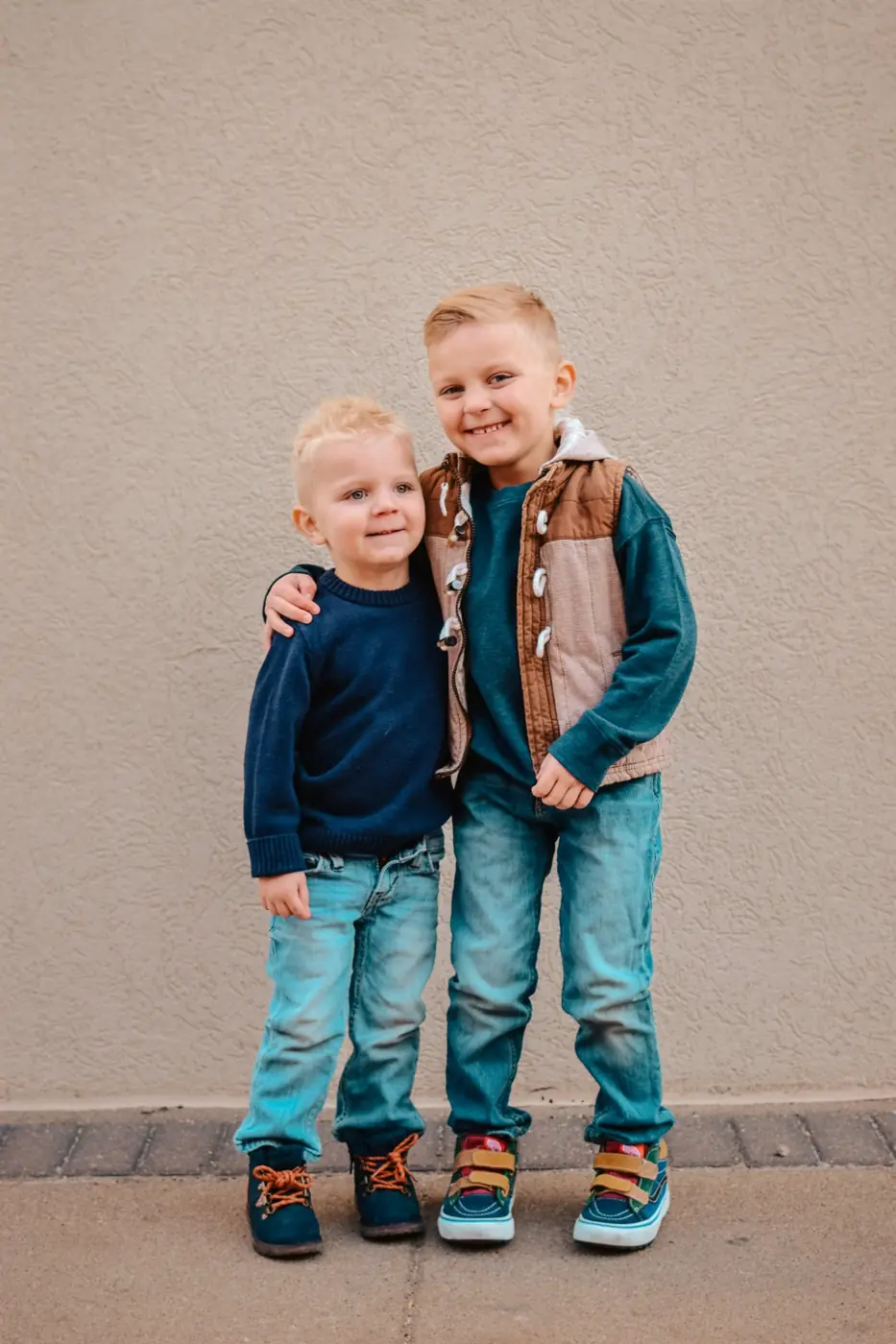 Two little brothers hugging in front of a textured wall