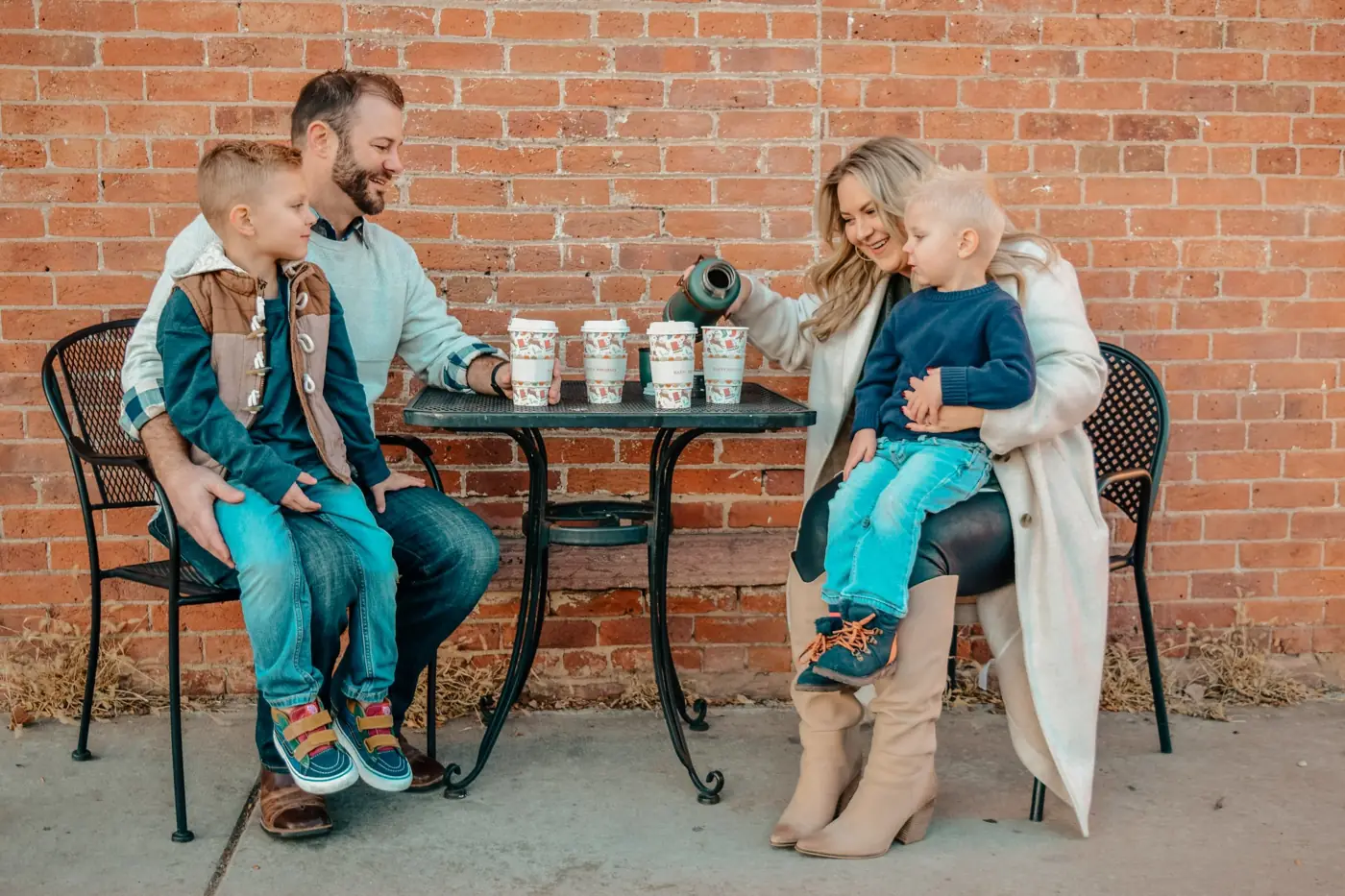 Family sharing hot cocoa at a cafe table by a brick wall