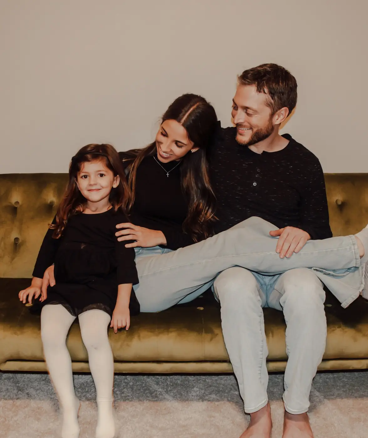 Mom, dad and daughter laughing together on a green velvet couch