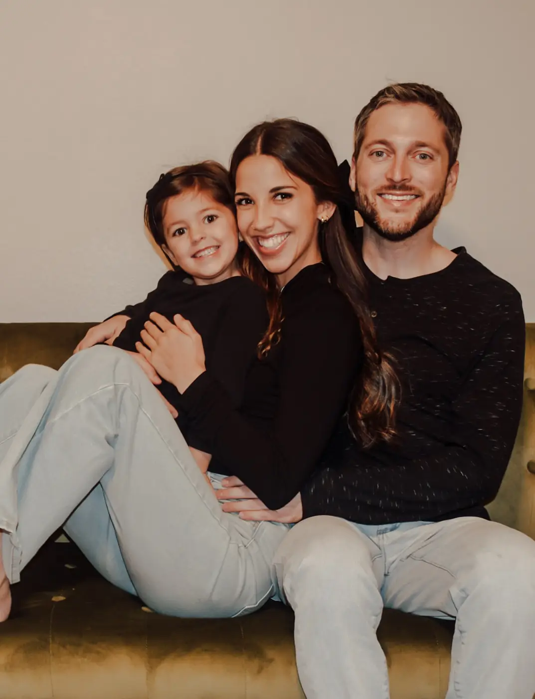 Family snuggled on a green velvet couch, all smiling at the camera