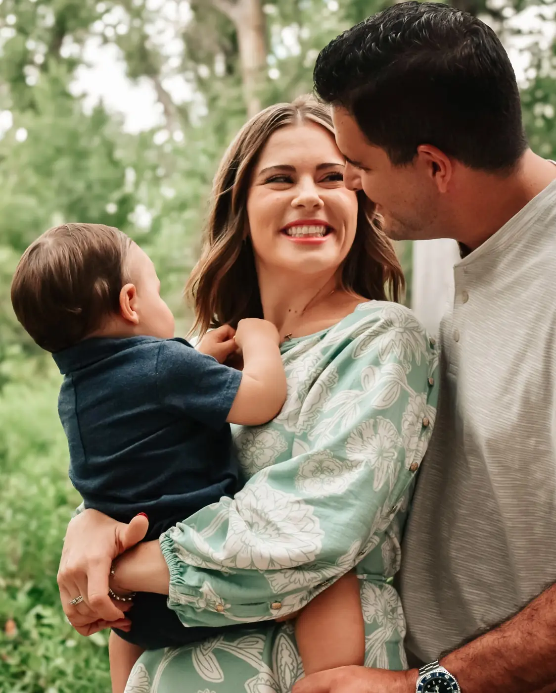 Mom laughing with her baby in her arms as dad kisses her cheek
