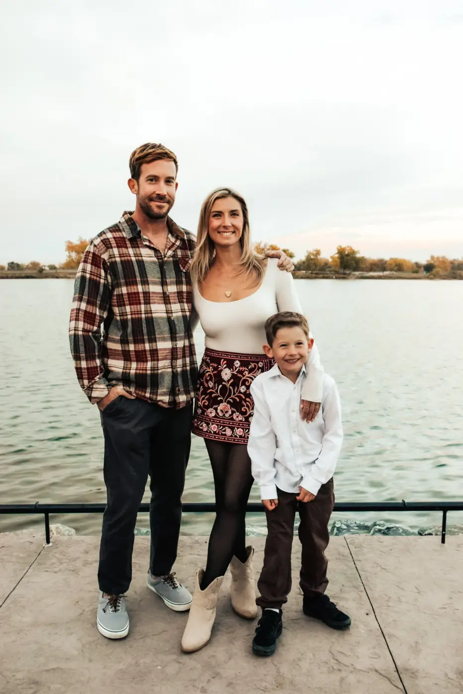 Family of three standing together by the lake at sunset