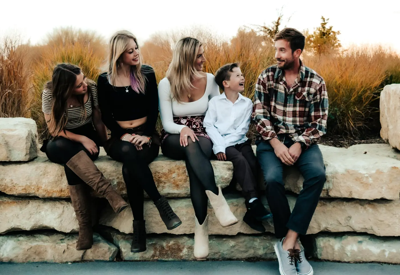 Family sitting on a stone bench laughing in golden grass