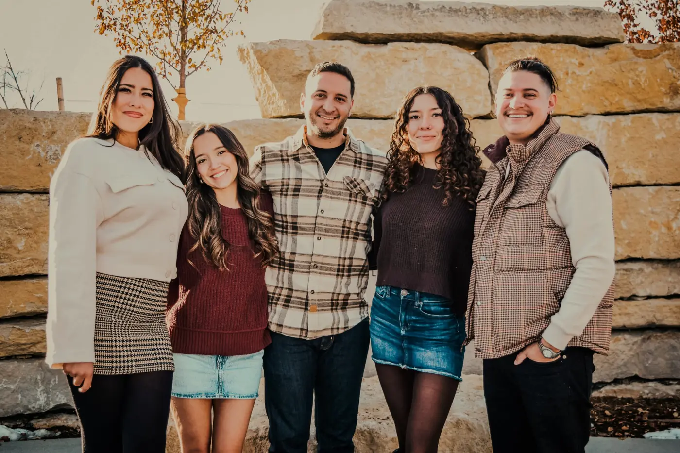 Five adult siblings and parents smiling in front of a stone wall