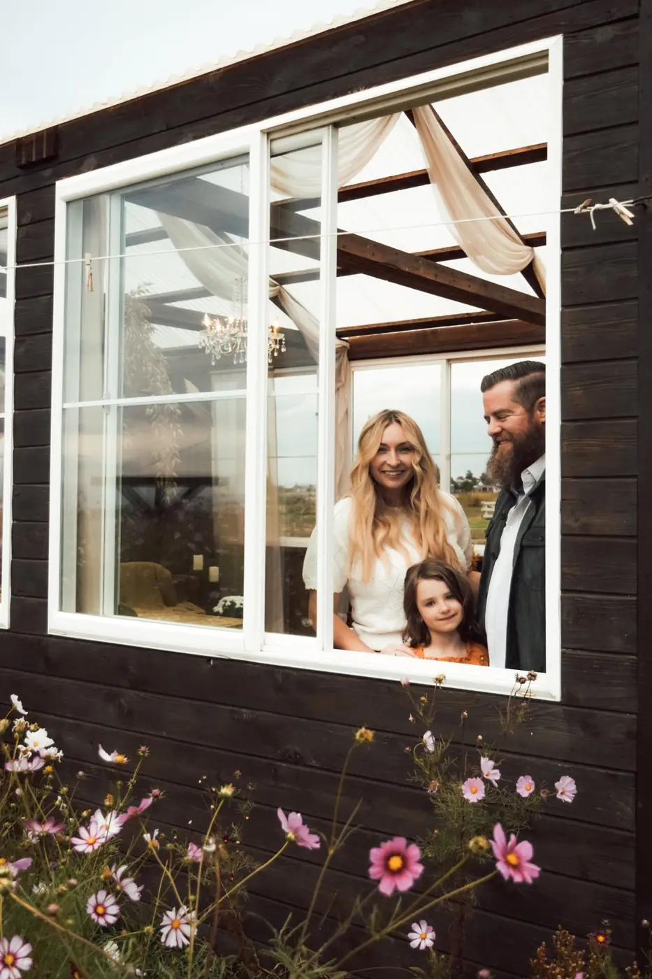 Family looking out of a window framed by pink cosmos flowers