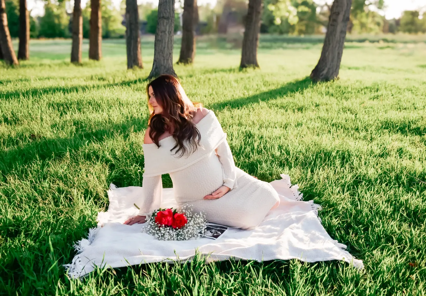 Expecting mother in a cream off-the-shoulder dress on a blanket with roses and an ultrasound photo
