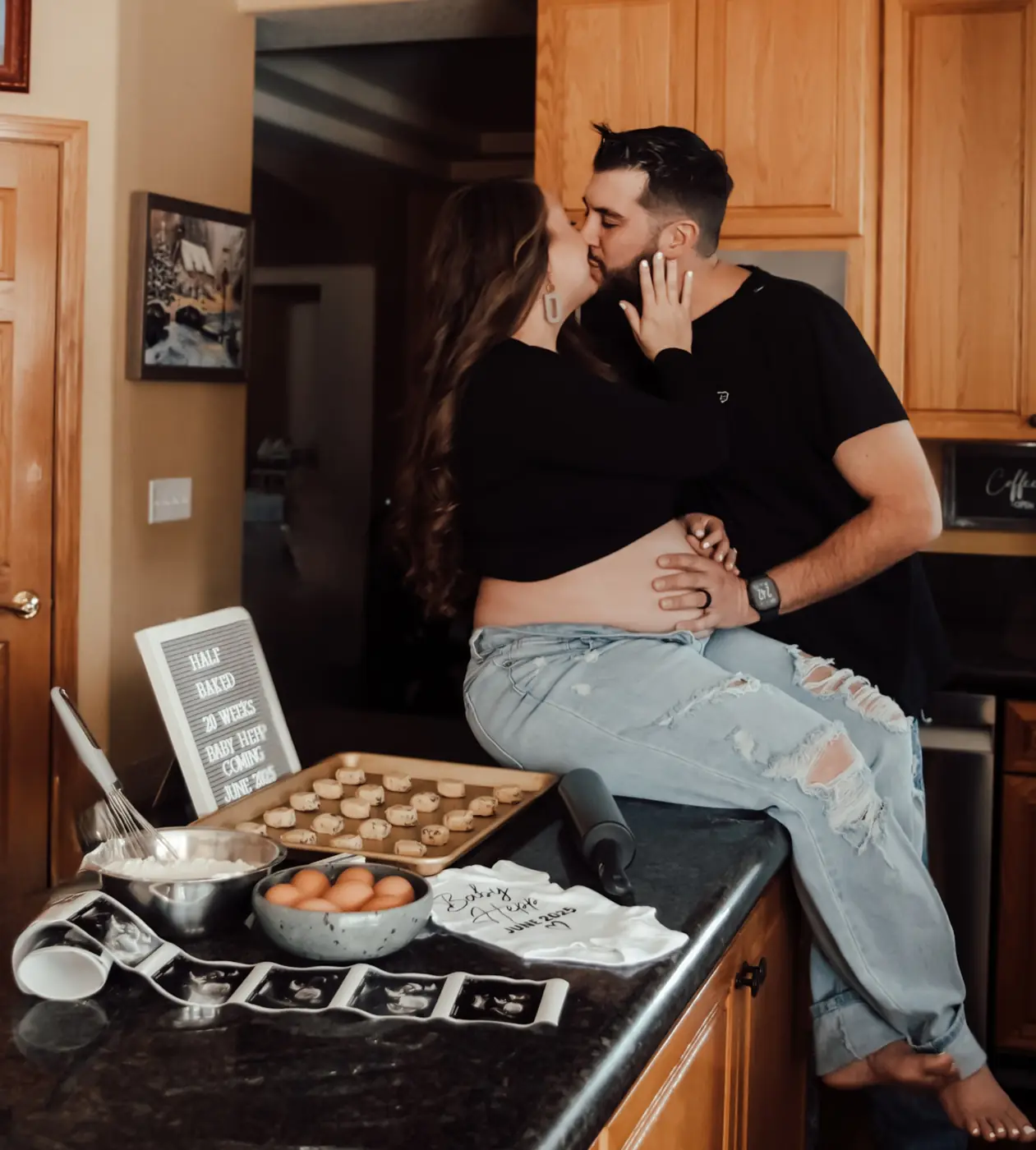Expecting couple kissing on the kitchen counter surrounded by baking props