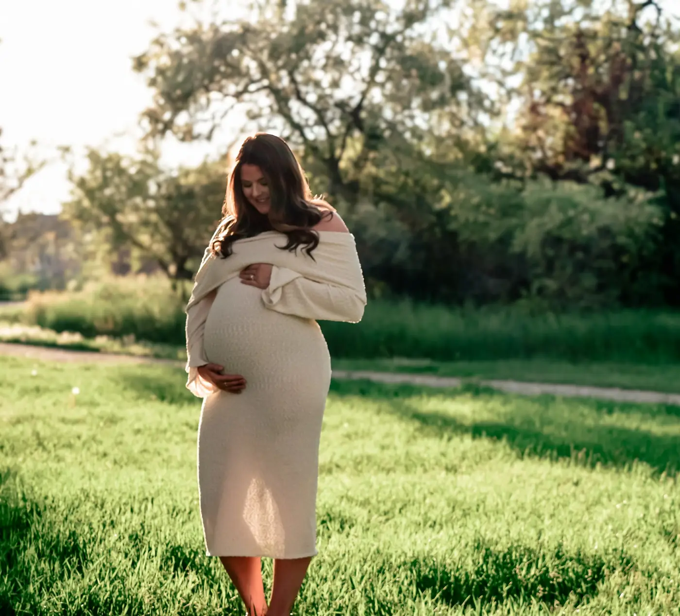Expecting mother in a cream off-the-shoulder dress glowing in the evening sun