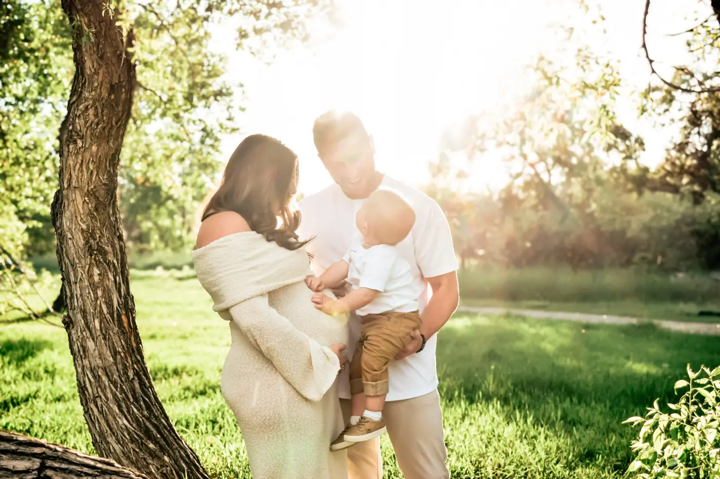 Expecting mother and dad holding their toddler in glowing golden sunlight