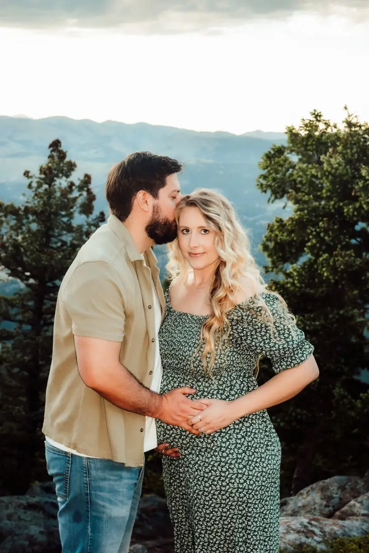 Expecting couple at a mountain overlook, he kisses her forehead