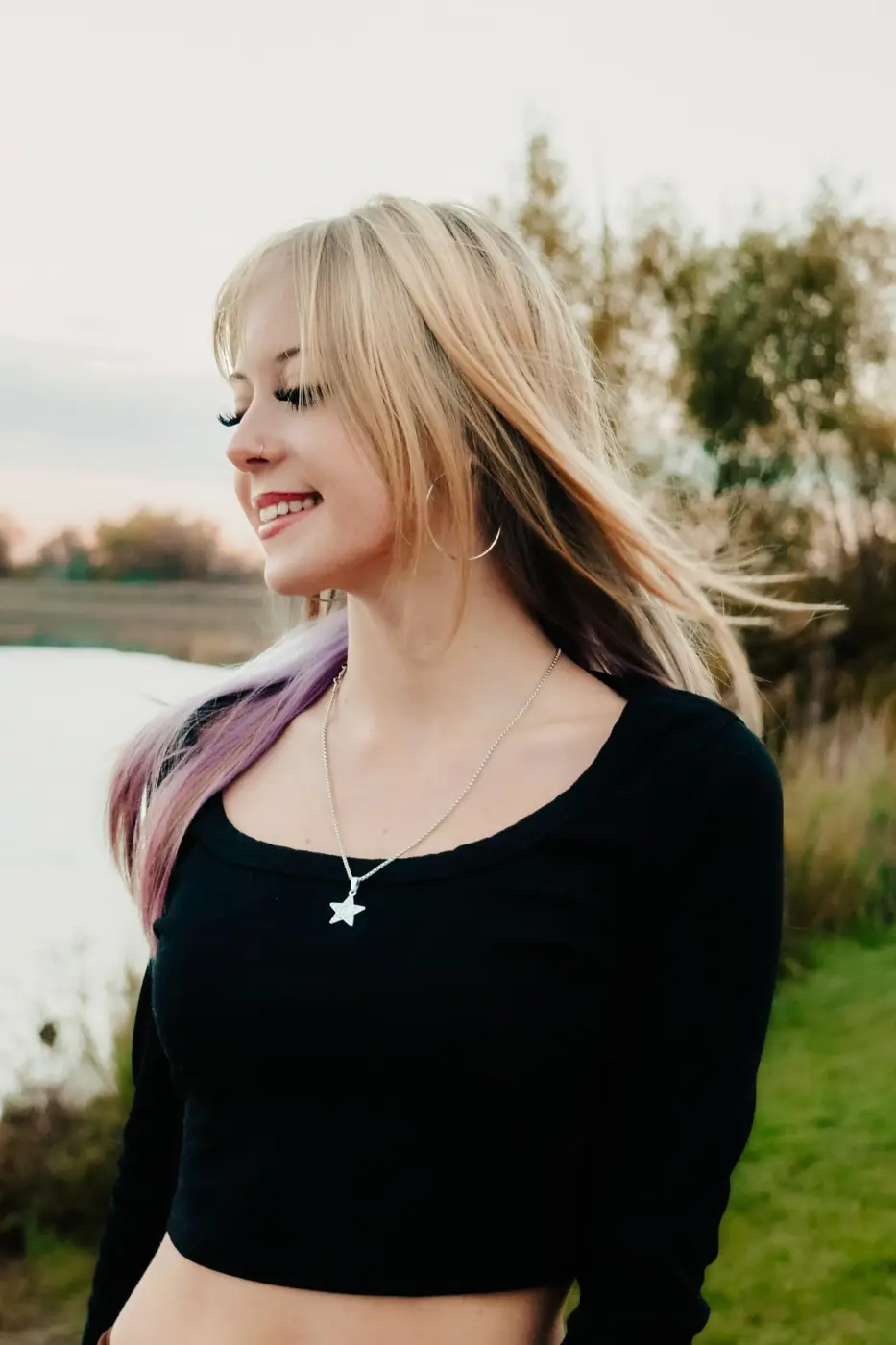 Senior girl with blonde and lavender hair laughing by the water in golden light
