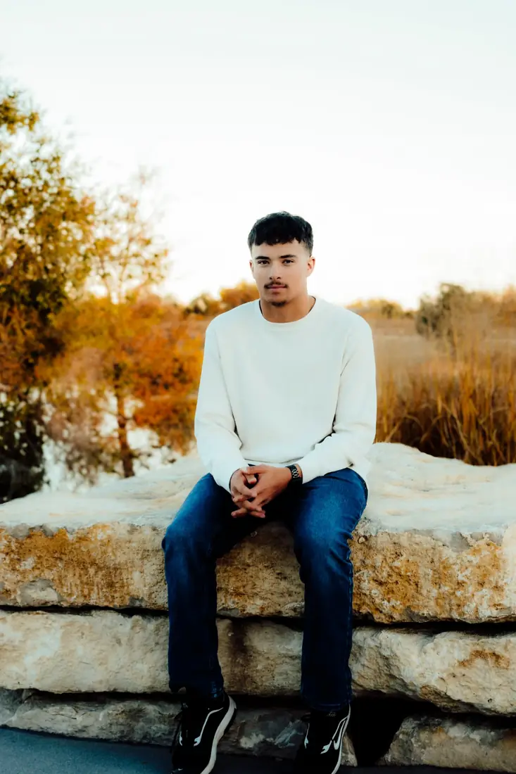 Senior portrait of a young man in a cream sweater on a stone wall
