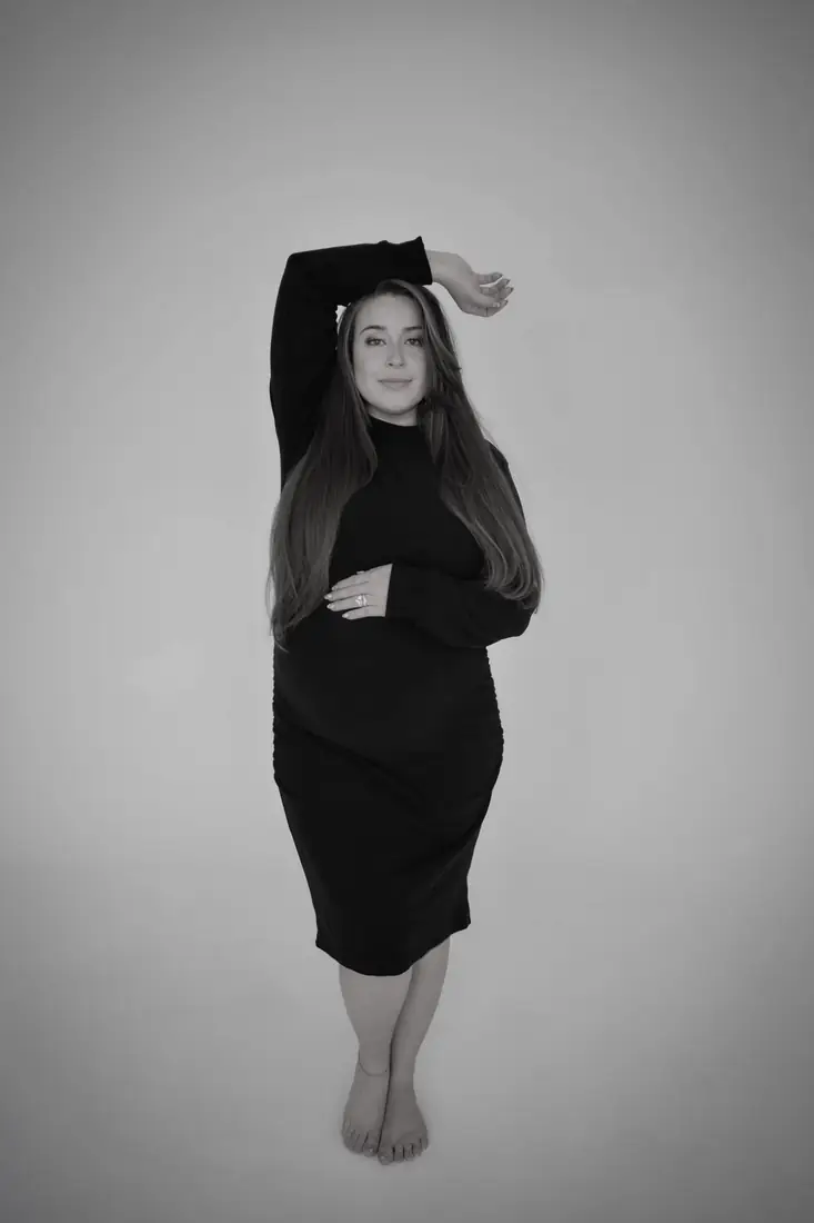 Black-and-white studio maternity portrait, arm raised overhead