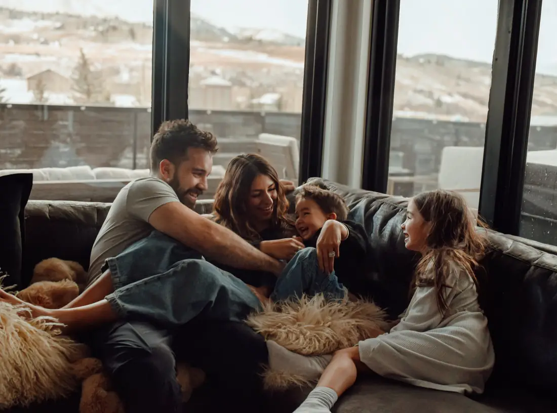 Family laughing together on a couch by big windows